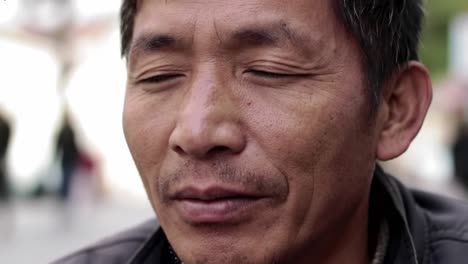 a man with closed eyes sits contentedly on a busy street, taking in the sounds and atmosphere around him. his calm demeanor contrasts with the lively environment, creating a reflective moment.