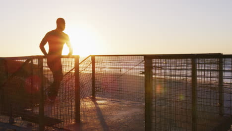 hombre afroamericano enfocado corriendo por las escaleras, haciendo ejercicio al aire libre junto a la playa al atardecer