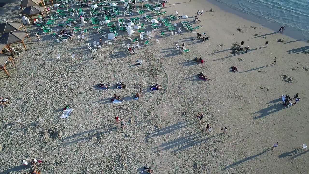 A beach scene with many people laying on the sand.