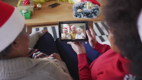 African-american-mother-and-daughter-using-tablet-for-christmas-video-call-with-family-on-screen