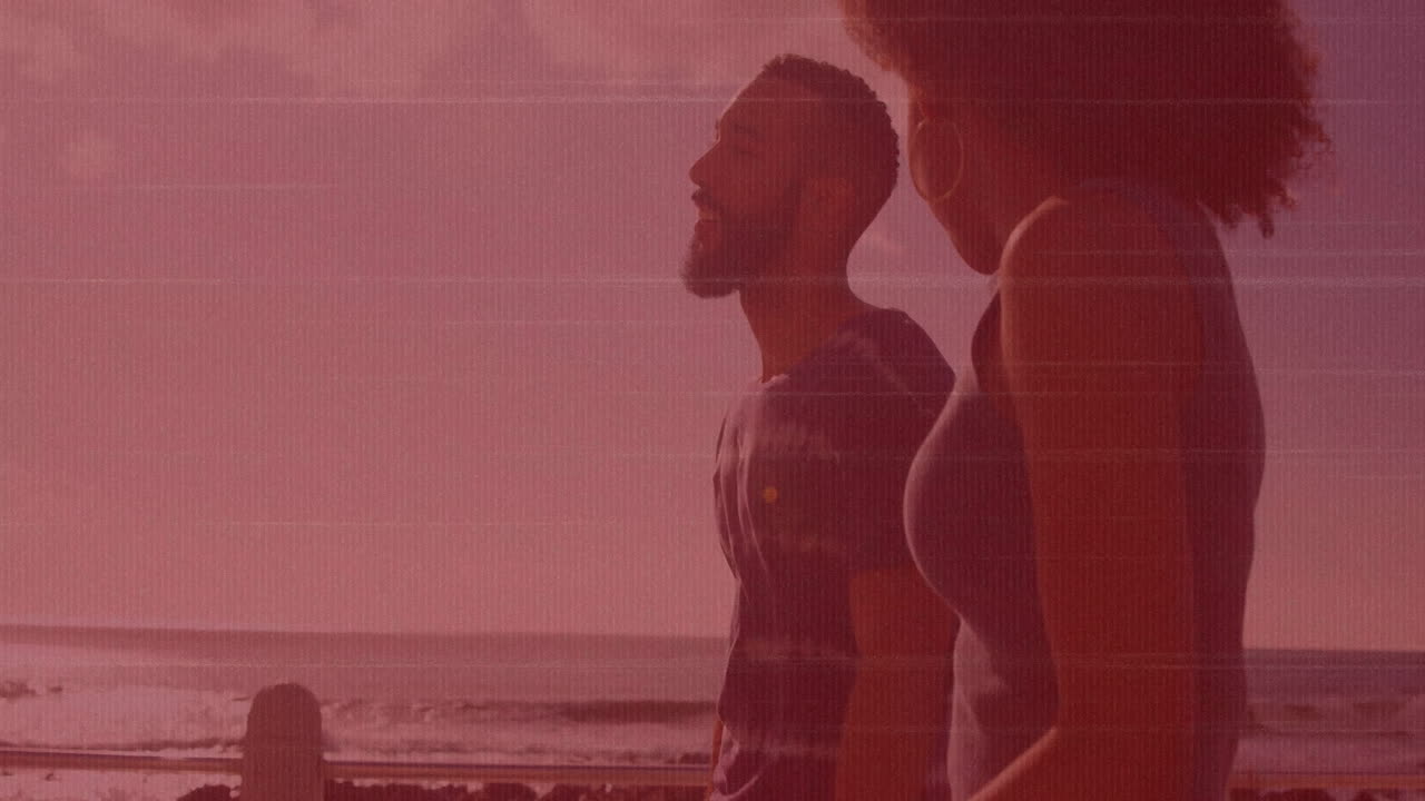 Walking on beach, couple under pink sky with ocean waves behind them