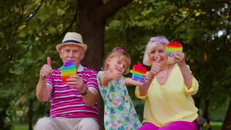 Ältere-Großmutter,-Großvater-Und-Enkelin-Halten-Anti-Stress-Pop-It-Spielzeugspiele-Im-Park