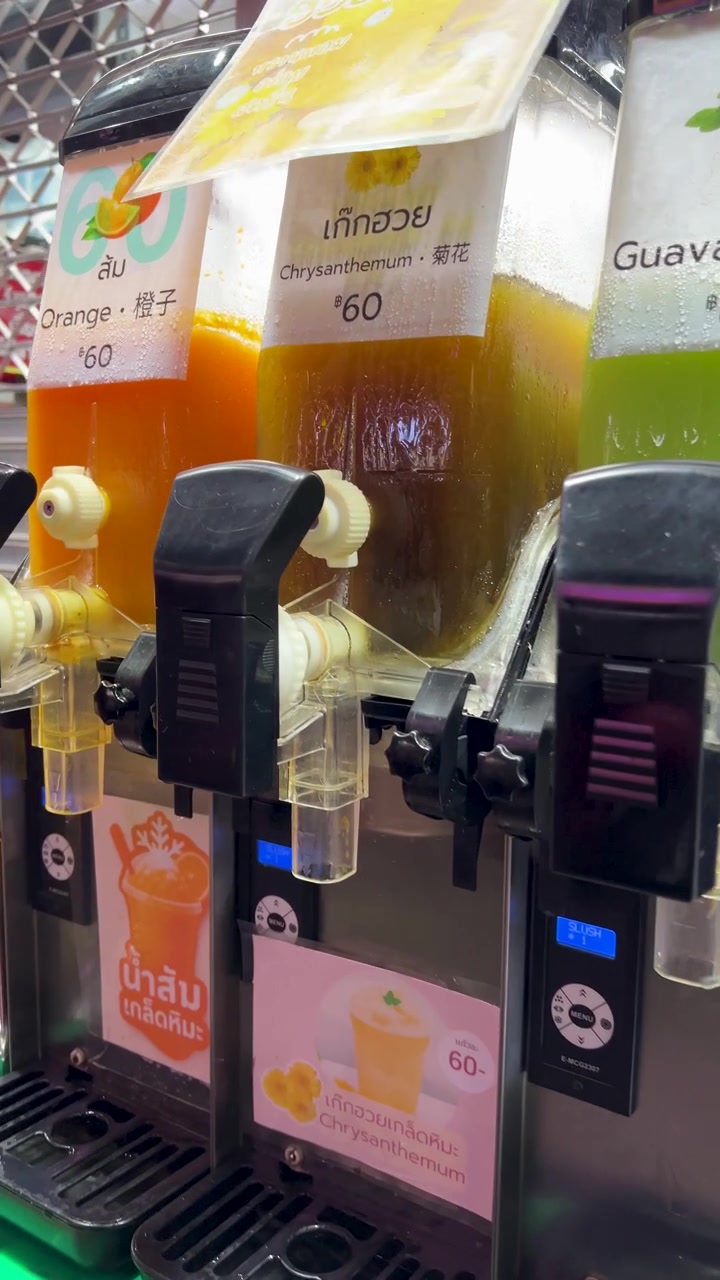 Brightly lit juice dispensers with guava, orange, and chrysanthemum drinks at night market