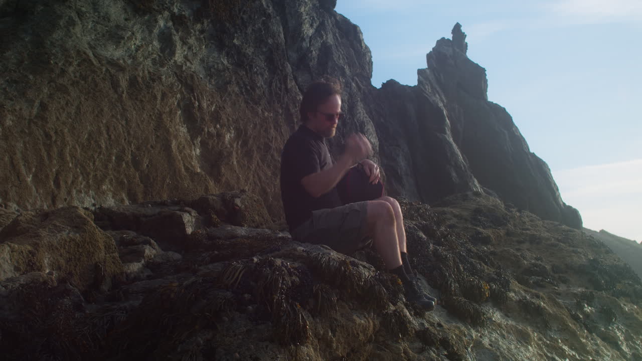 Man Sitting On The Rocky Coast Admiring The Seascape At Sunset. - static