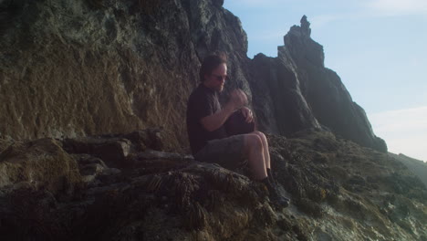 man sitting on the rocky coast admiring the seascape at sunset. - static