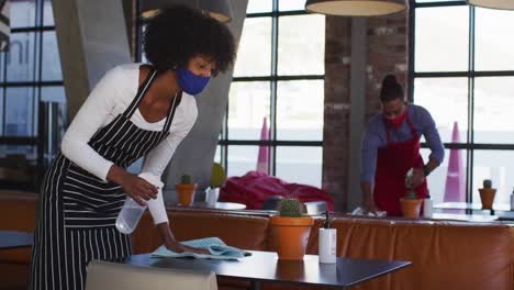 Diverse-cafe-workers-wearing-face-masks-disinfecting-tables