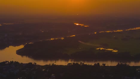 timelapse of a golden sunset over a foggy rural countryside, with small boats sailing down the river