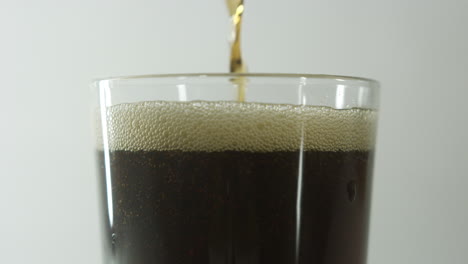 cola se vierte en un vaso con solo la parte superior del vaso a la vista contra un fondo claro y liso