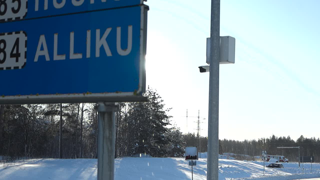 Roadside view of traffic sign in Laagri as melting snow drips down, creating water splatter and slow motion droplets. sun shines behind the road sign. Snow covered road landscape and winter conditions