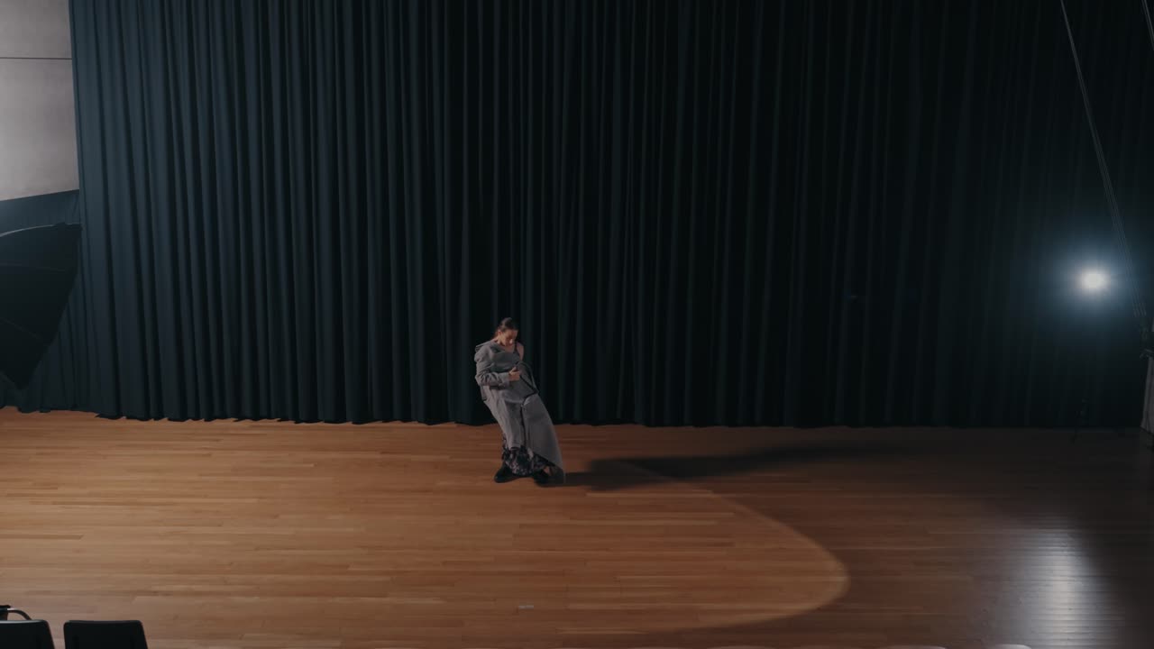 bailarín solo con un traje gris moviéndose en el escenario con un foco