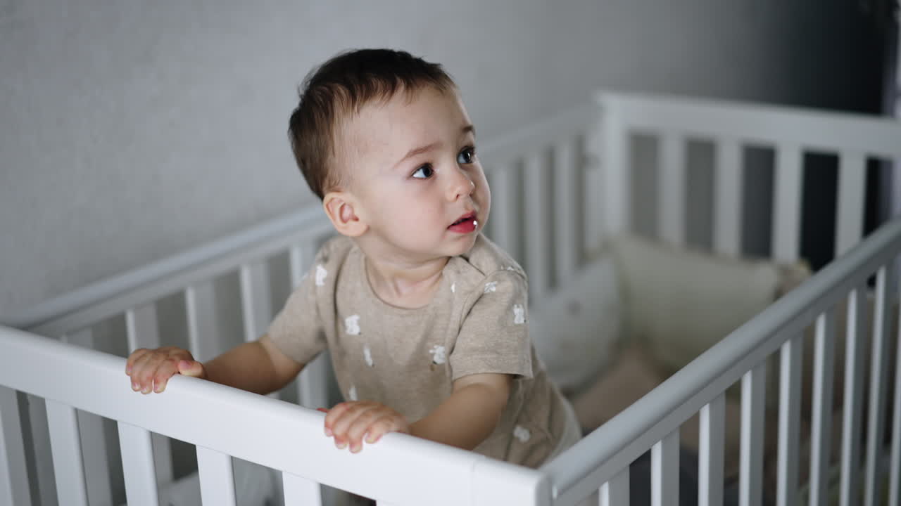 Un bambino piccolo attivo sta nella sua culla. Il bambino si tiene alle sponde e salta eccitato scuotendo il lettino.