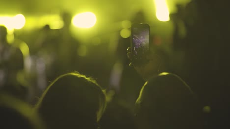 hands in the crowd of unrecognizable people holding smart phone and shooting musical performance. bright illumination on the stage