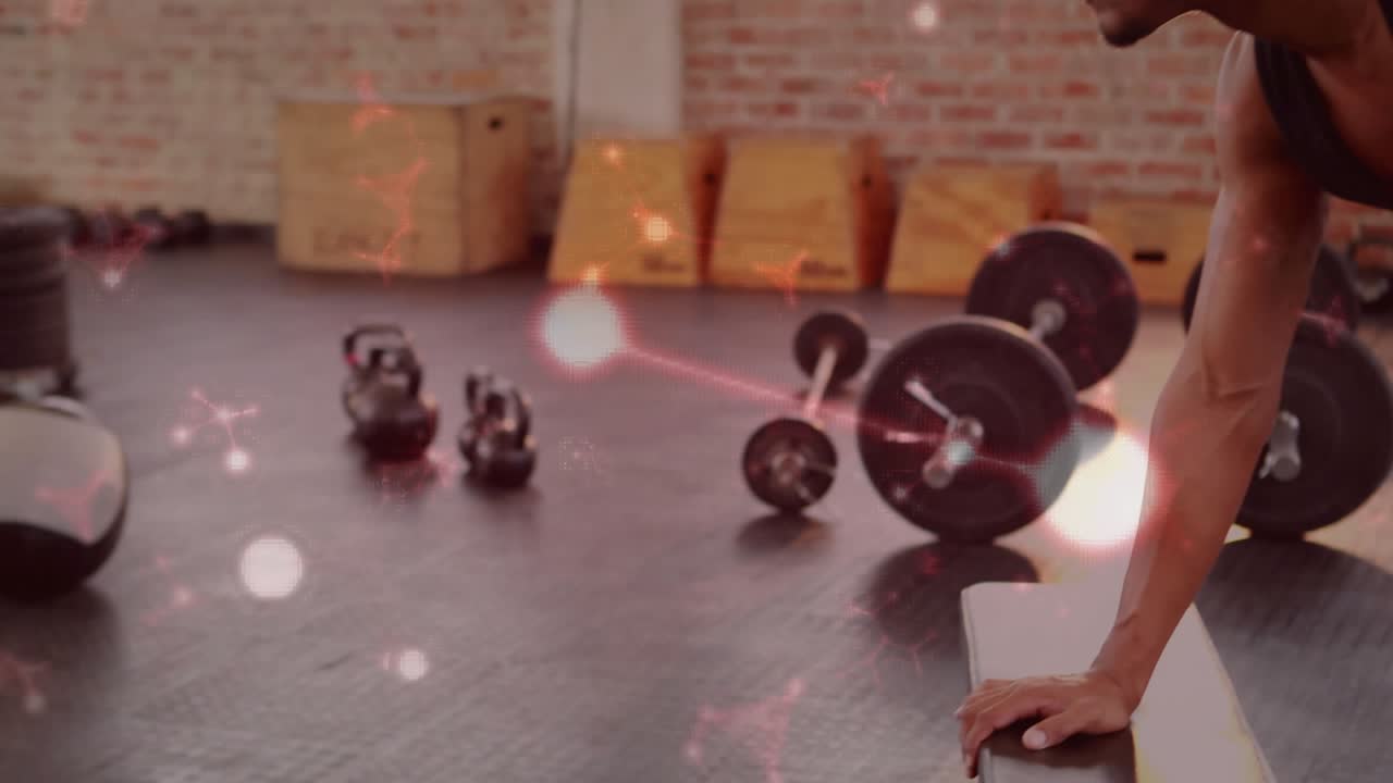 Man bracing on step, reaching for dumbbell, doing one-arm row in gym, bokeh accenting back strength