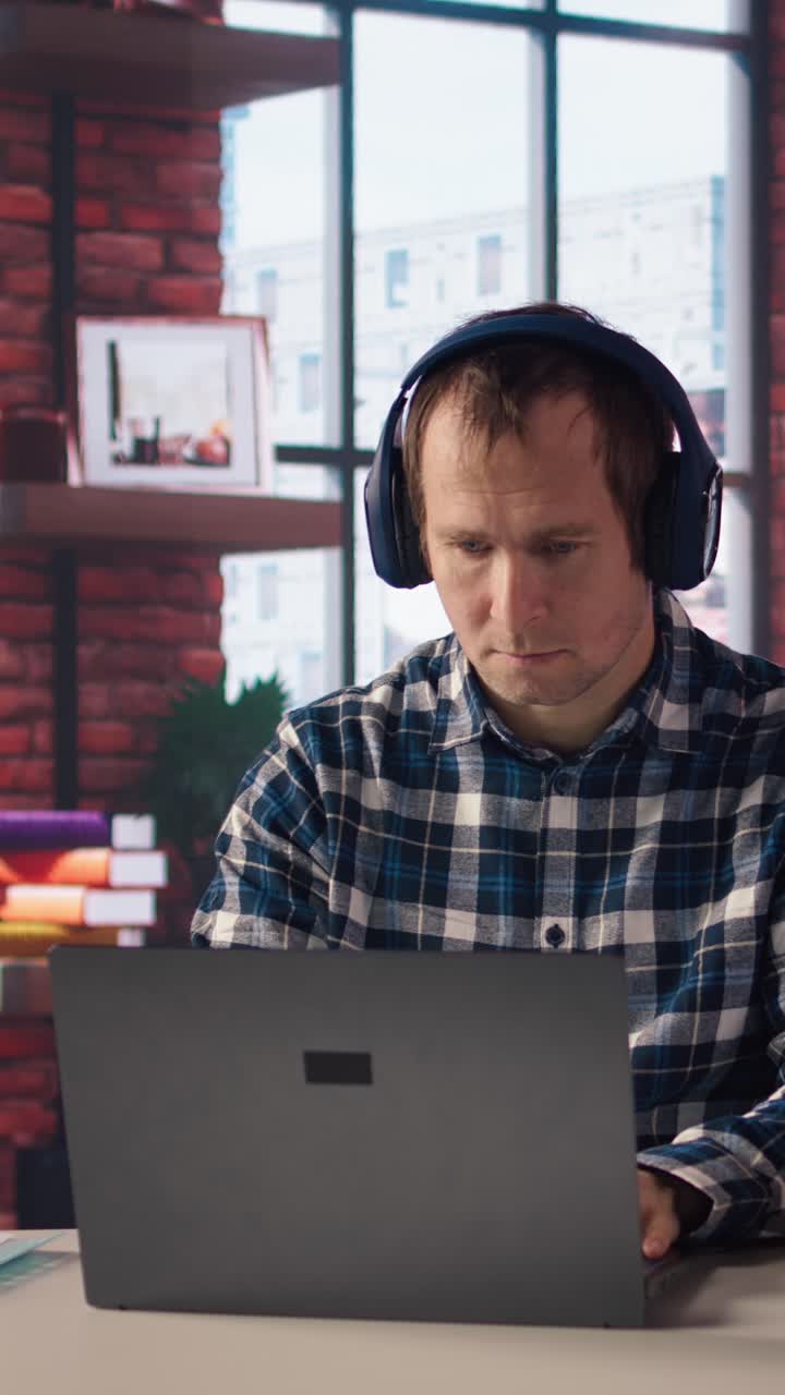 Vertical video Worker listening music, analyzing data on laptop at desk