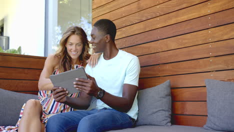 smiling diverse couple sitting on couch using tablet, enjoying time together