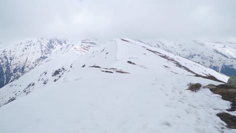 POV-Eines-Bergsteigers-Auf-Einem-Schneebedeckten-Bergrücken-Mit-Blick-Auf-Den-Von-Wolken-In-Der-Ferne-Verdeckten-Gipfel