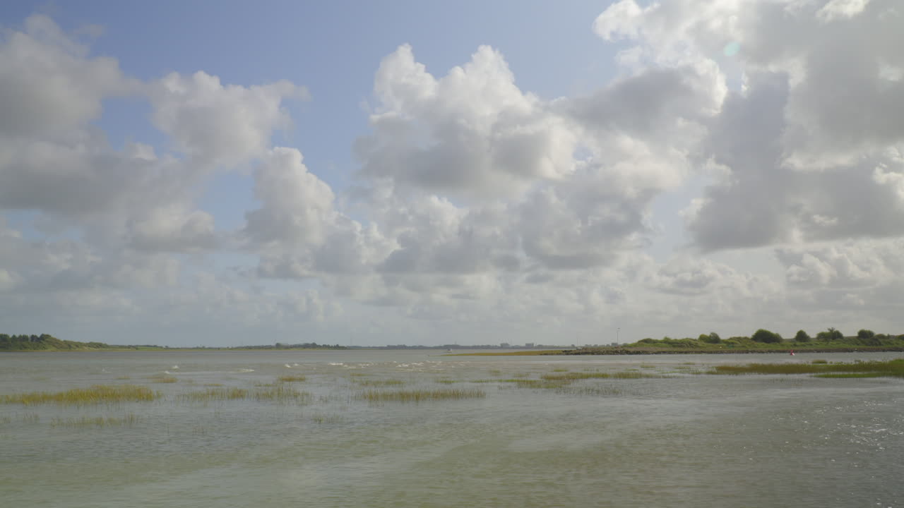 강 입구의 조류가 후퇴하여 소금 습지를 드러내고, 밝은 구름이 늦은 여름 오후에 수평선에서 날아갑니다.