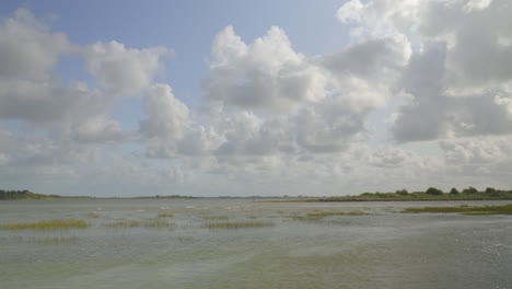 river estuary tide receding revealing salt marsh, as bright clouds fly by on the horizon on a late summer afternoon