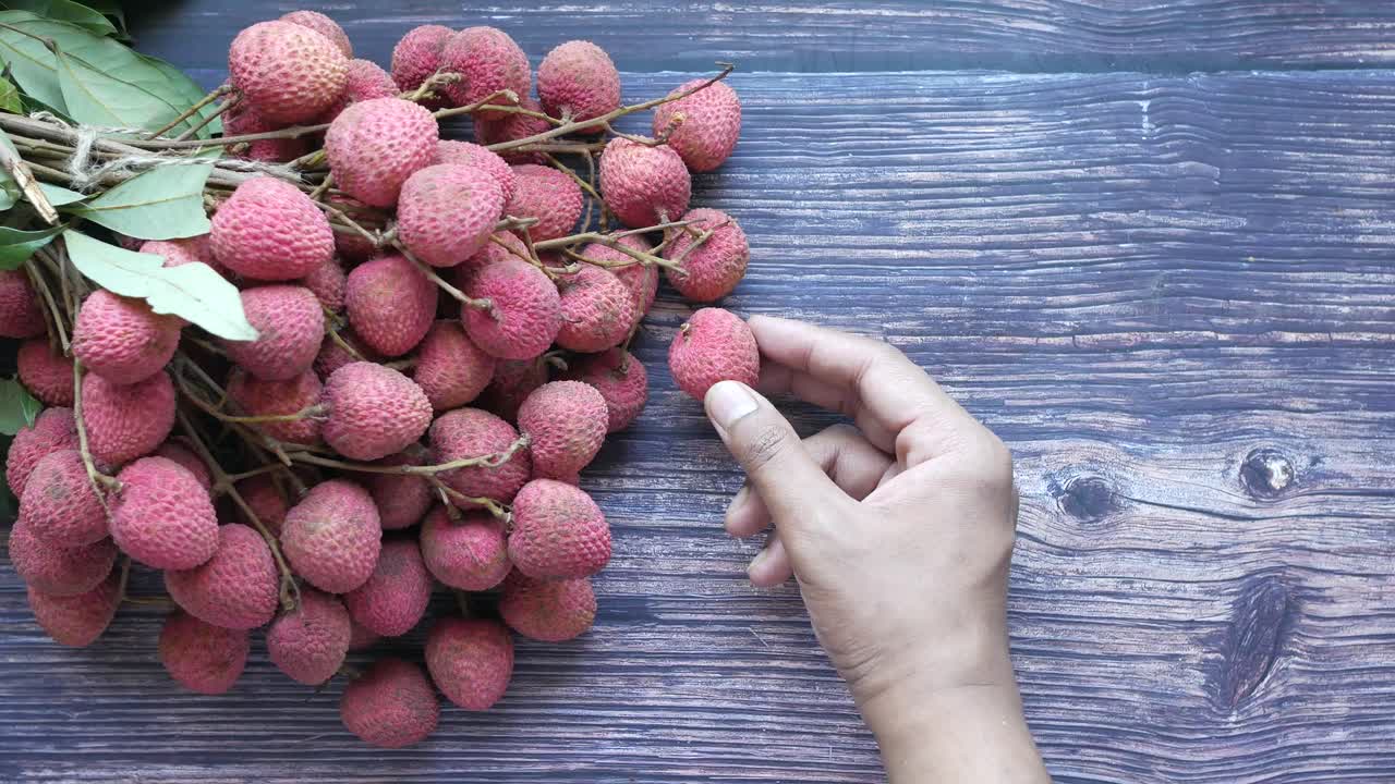 Tangan memegang buah leci di atas meja kayu