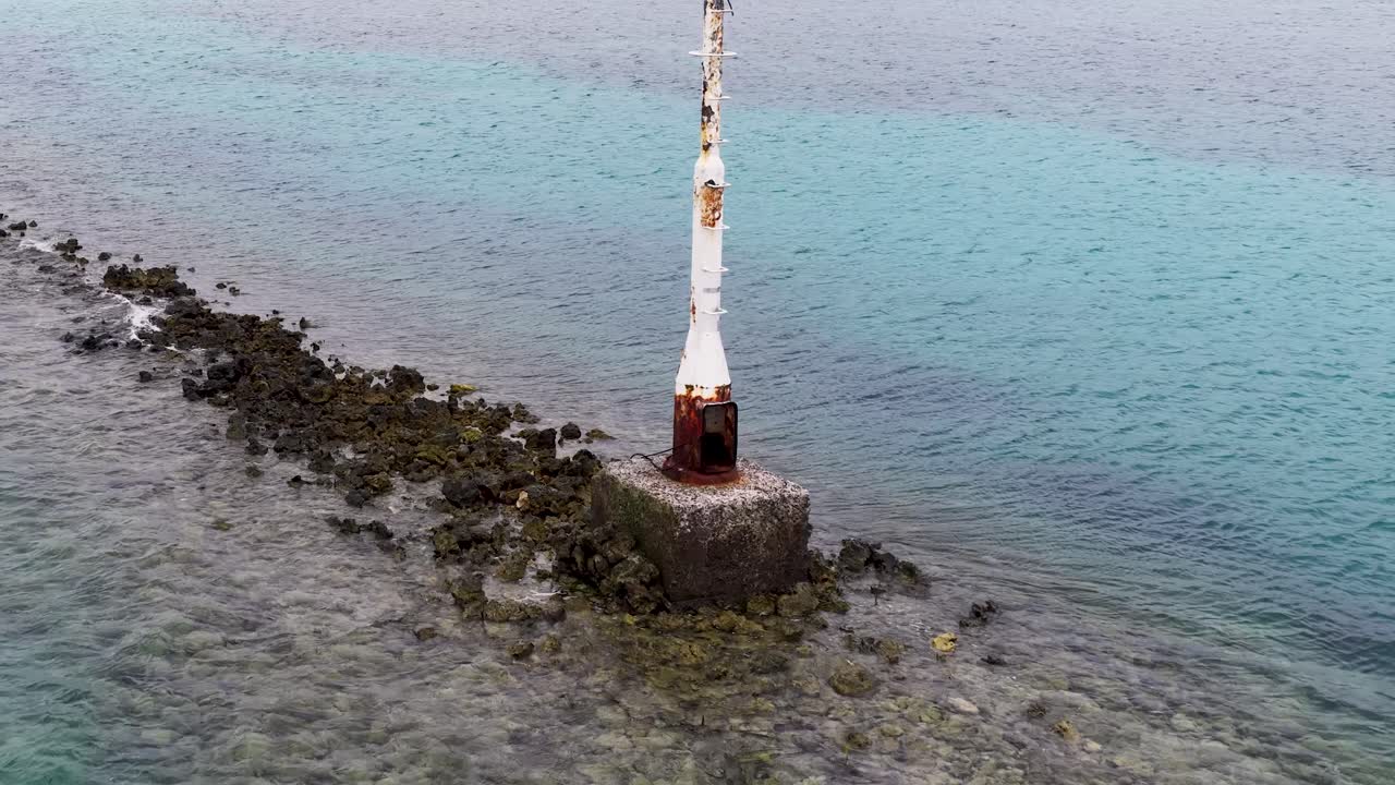 Un drone orbita attorno a un segnale di navigazione usurato lungo una costa rocciosa vulcanica nelle acque turchesi del Pacifico