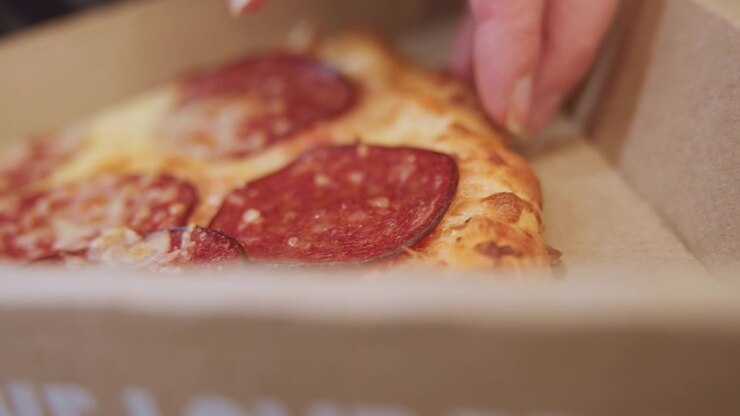 Cartone di pizza vuoto che mostra macchie di grasso, briciole sparse dopo un pasto da asporto, spuntino notturno in ufficio, avanzi di festa; primo piano dell'interno di cartone testurizzato con segni di olio e illuminazione suggestiva