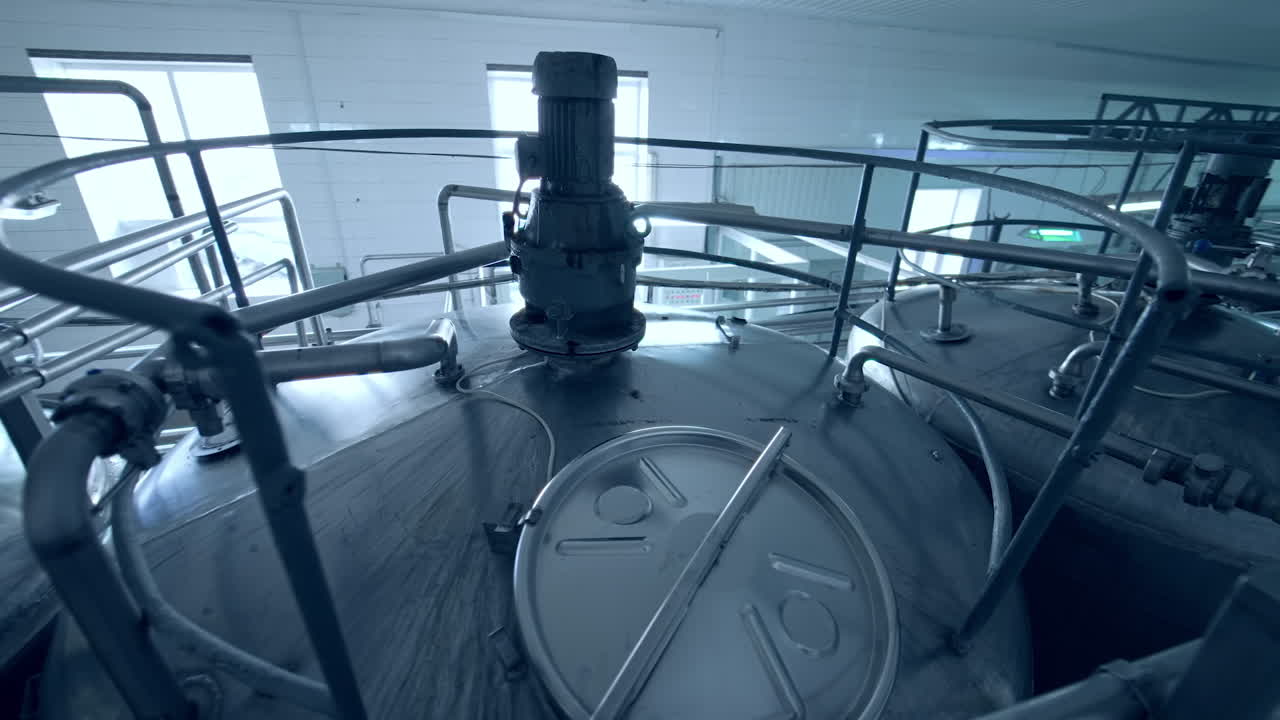 Big steel tanks standing in a row at the dairy plant. The look at the tops of milk cisterns from above. Gaze from a bridge leading to the cistern lids.