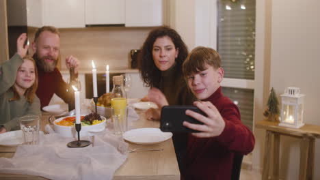 niño rubio sentado con su hermana y sus padres en la mesa de la cena de navidad usa un teléfono inteligente para hacer un selfie familiar 2
