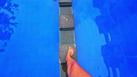 woman feet walking over swimming pool steps carefully, clean water reflection