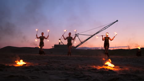 Professional-artists-show-a-fire-show-at-a-summer-festival-on-the-sand-in-slow-motion.-Fourth-person-acrobats-from-circus-work-with-fire-at-night-on-the-beach