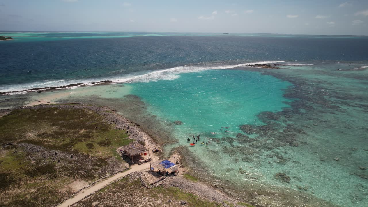 Turquoise waters meet rocky shore as people swim near Pisina Franky, a remote tropical destination