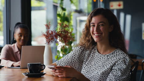 Retrato-De-Una-Joven-Empresaria-Sonriente-Sentada-En-Una-Cafetería-Usando-Un-Teléfono-Móvil