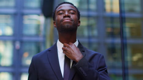 retrato de un joven empresario confiado ajustando un traje de pie fuera de las oficinas en el distrito financiero de la ciudad de londres, reino unido.