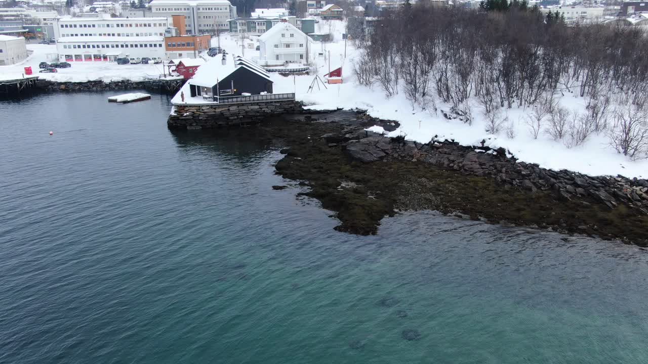 Drone still view in Tromso area flying over sea in winter looking at Finnsnes small town with a hotel on the shore in Norway