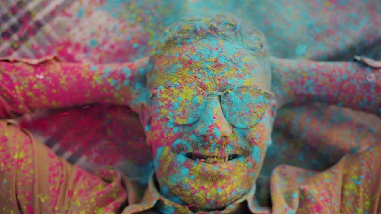 Top view of Middle Eastern man lying on blanket outdoors and gulal powder paint falling on him at Holi festival
