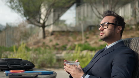 Sitted-man-in-formal-suit-eating-organic-nuts-from-plastic-container-outdoors-in-city-park