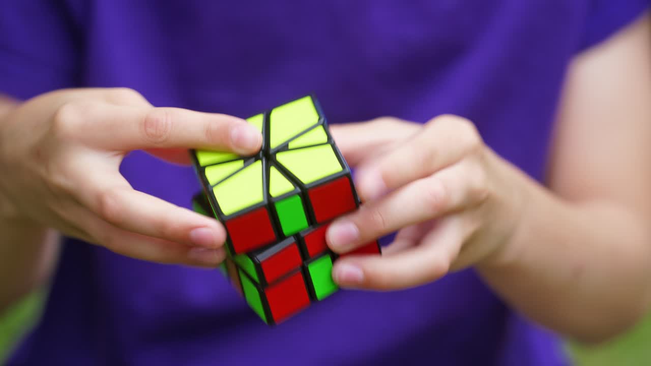 Boy's hands solving Rubik's Cube. Clever child holding Rubiks cube and doing quickly interesting puzzle game. Close-up of colorful cube in kid's hands.