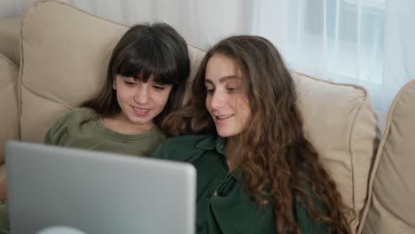 pareja de hermosas mujeres jóvenes alegres sonriendo mientras ven una película en el ordenador en el sofá