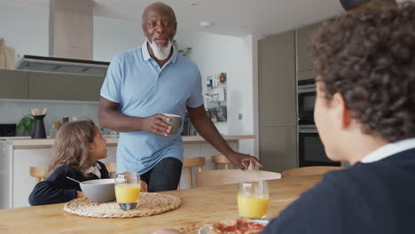 Grandparents-Sitting-In-Kitchen-With-Grandchildren-Eating-Breakfast-Before-Going-To-School