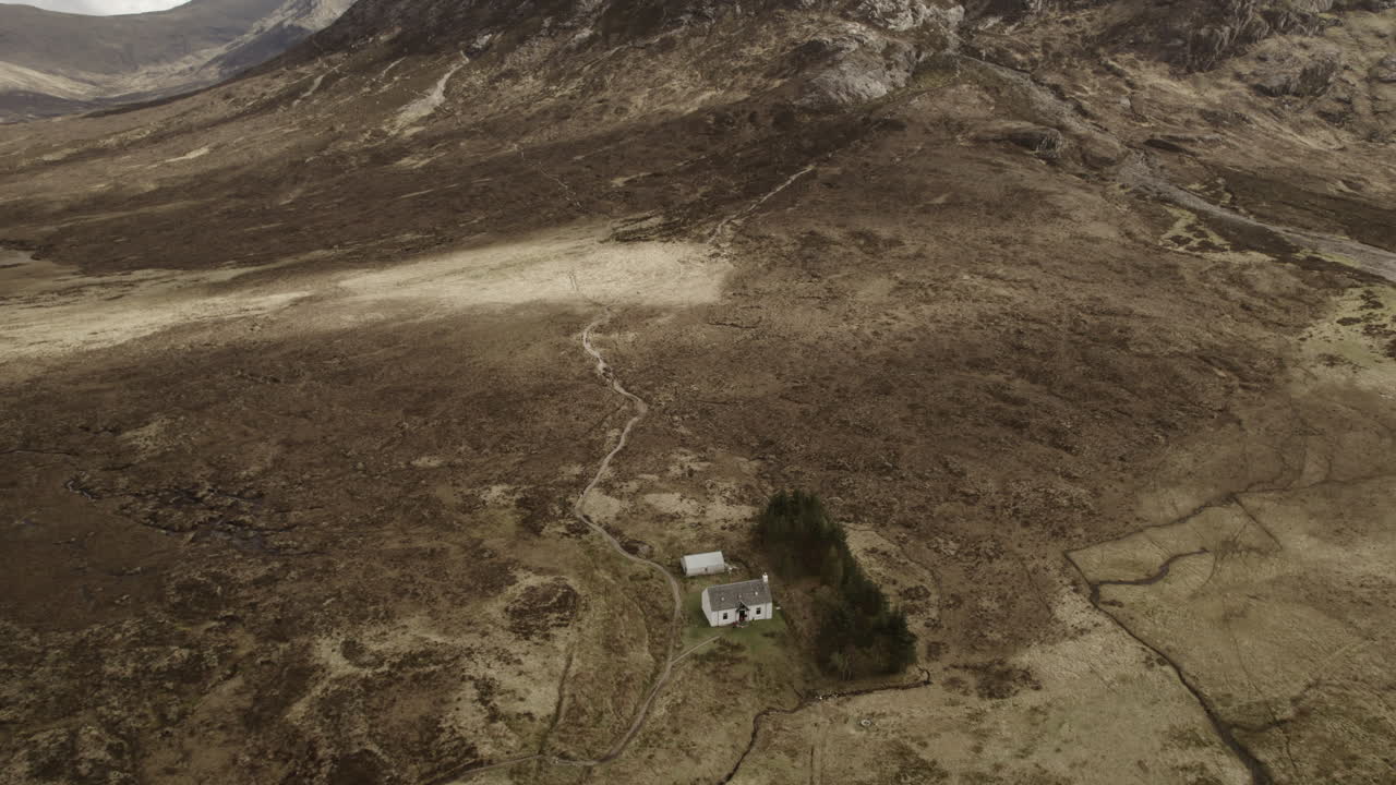 volando sobre una cabaña blanca de lagangarbh en las tierras altas escocesas de glencoe con la montaña buachaille etive mor en la distancia