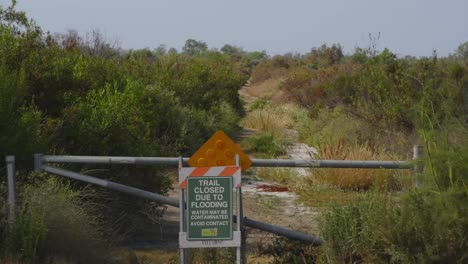 una señal de sendero cerrado advierte de inundaciones y contaminación potencial, enfatizando las fuerzas impredecibles y a veces peligrosas de la naturaleza