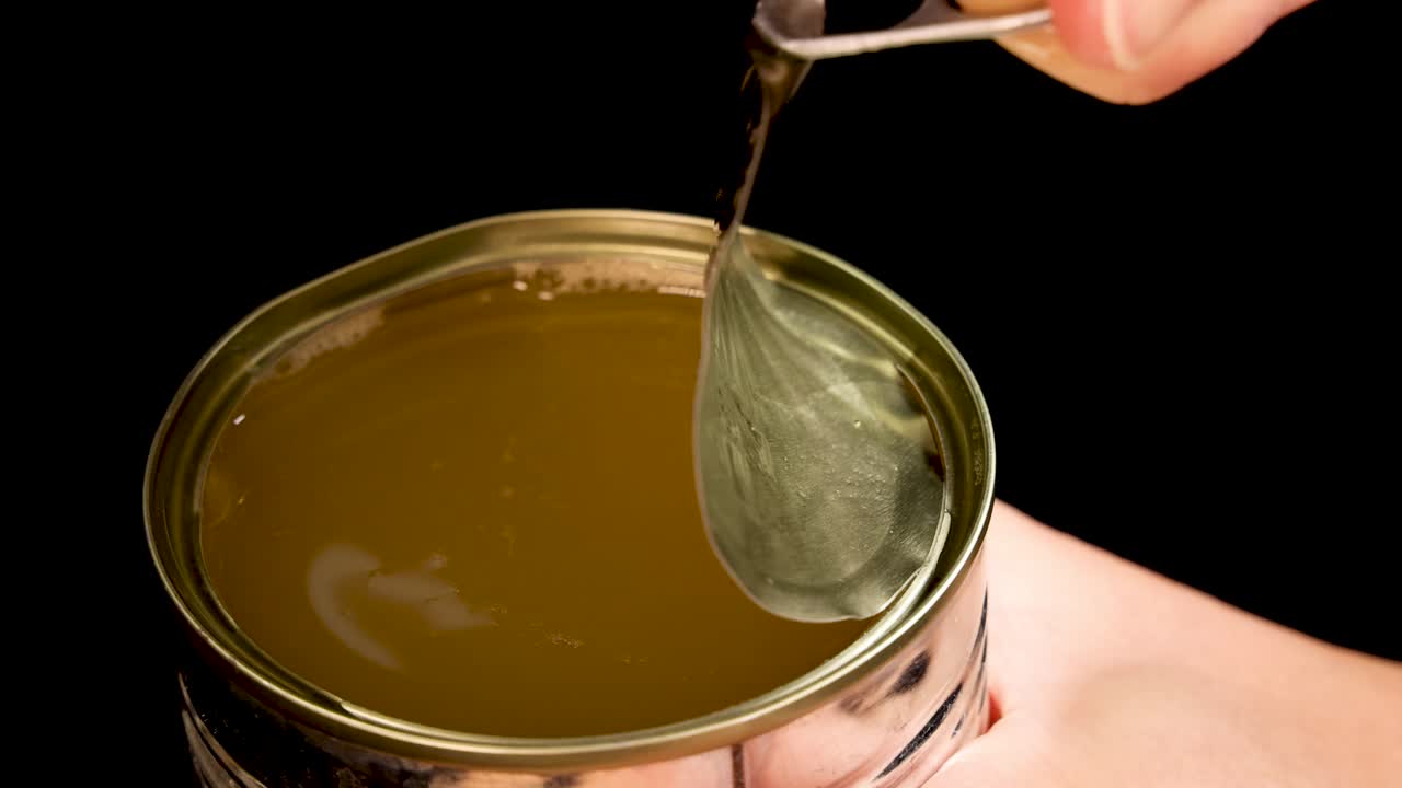 A hand uses a pull-tab to open a metal can filled with green beans in liquid, shot against a black background with even studio lighting