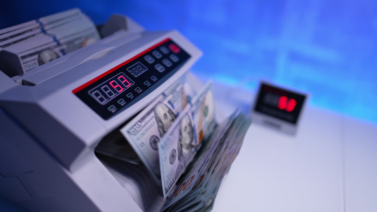 American money counted in the cash counting machine. Display of equipment shows quickly changing numbers. Close up. Blurred backdrop.