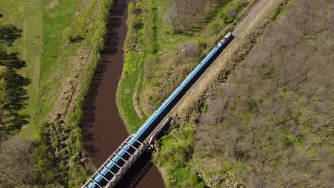 Toma-Aérea-Del-Tren-Azul-Que-Pasa-El-Puente-En-La-Zona-Rural-De-Buenos-Aires-Durante-El-Verano