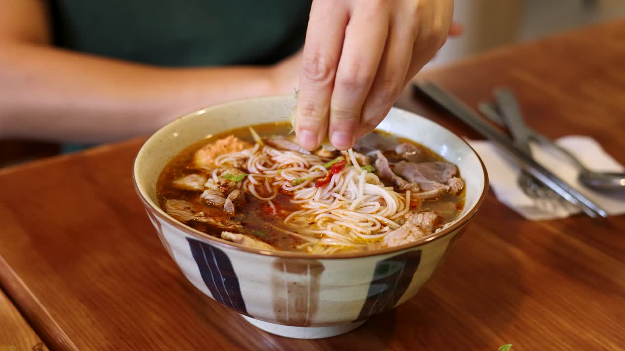 Primo piano di mani che spremono succo di lime sopra una ciotola di ceramica di zuppa di noodle vietnamita