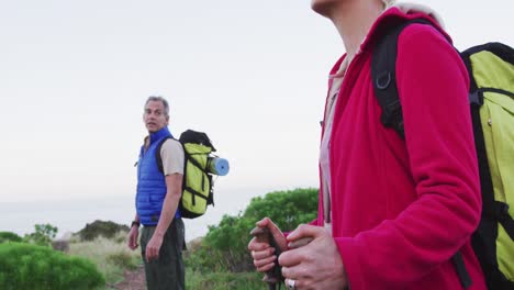 Senior-hiker-couple-with-backpacks-and-hiking-poles-looking-at-each-other-standing