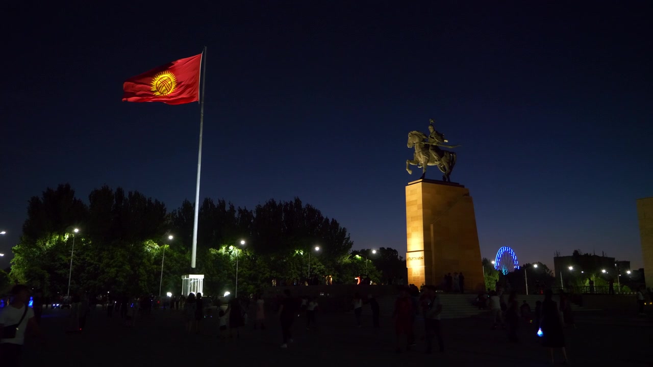 夜のアイコル・マナスの像とキルギスの国旗。