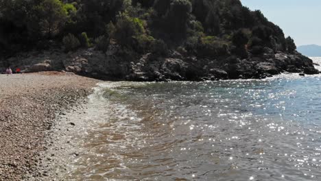 Ripples-of-water-at-low-tide-washing-up-against-a-pebble-beach,-Jerusalem-Beach,-Erisos,-Greece---drone-shot