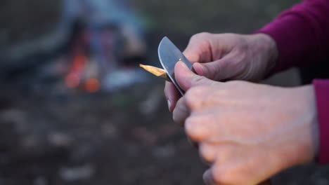 Young-woman-shapes-stick-into-a-point-with-knife,-outdoor-setting,-slow-motion