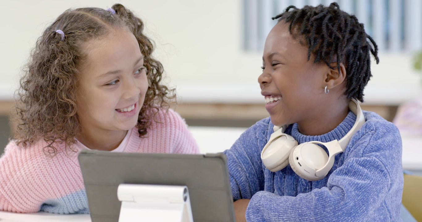 Diverse teen female friends leaning in watching tablet content laughing together at white table