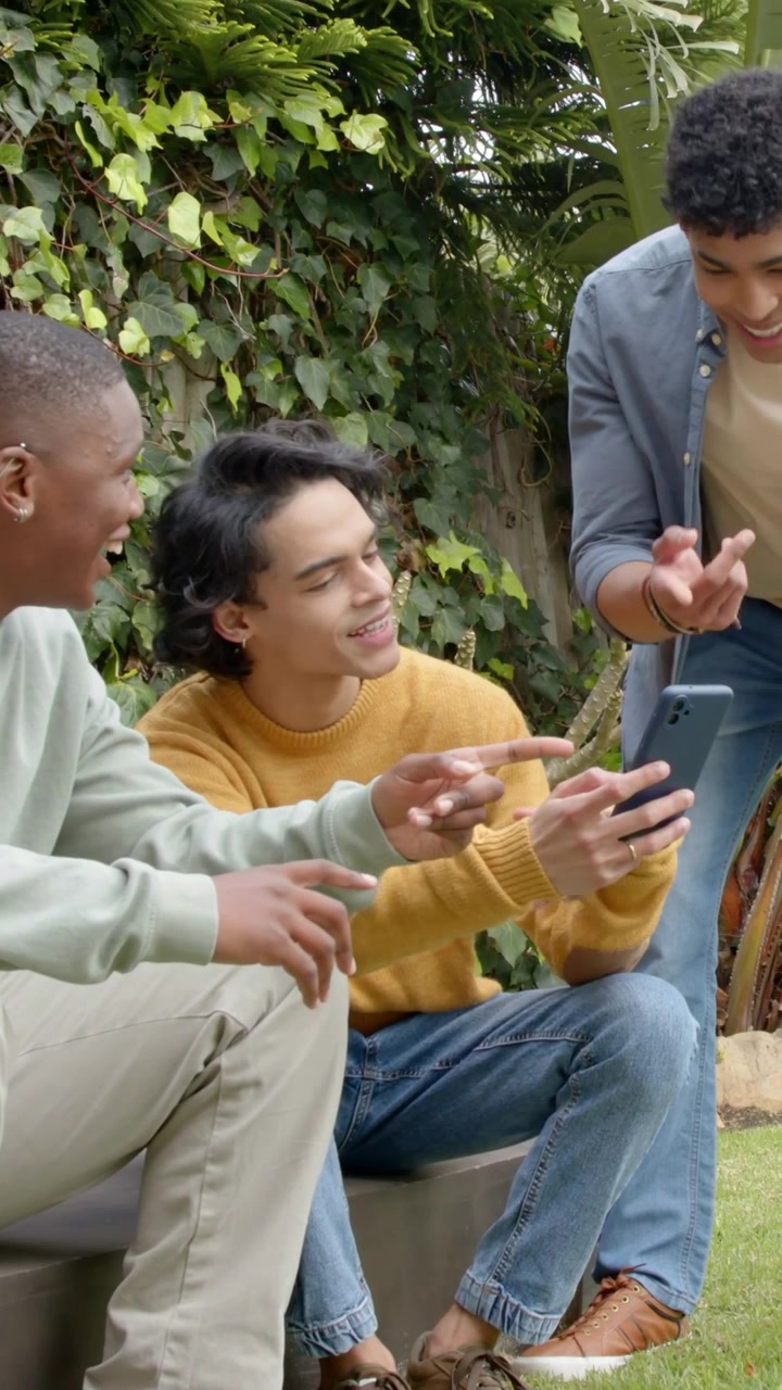 Vertical video: Holding smartphone center man in mustard knit showing content for friends in garden